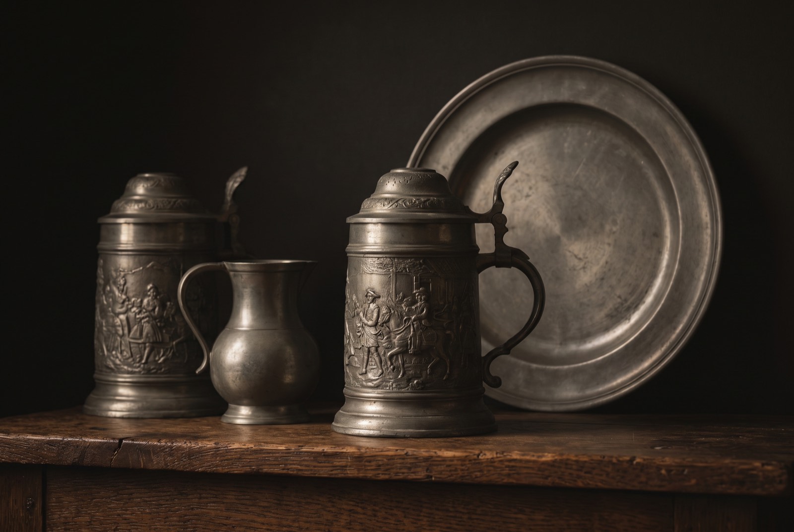 Zinnkrüge, Zinnkanne und Zinnteller auf altem Eichenholz